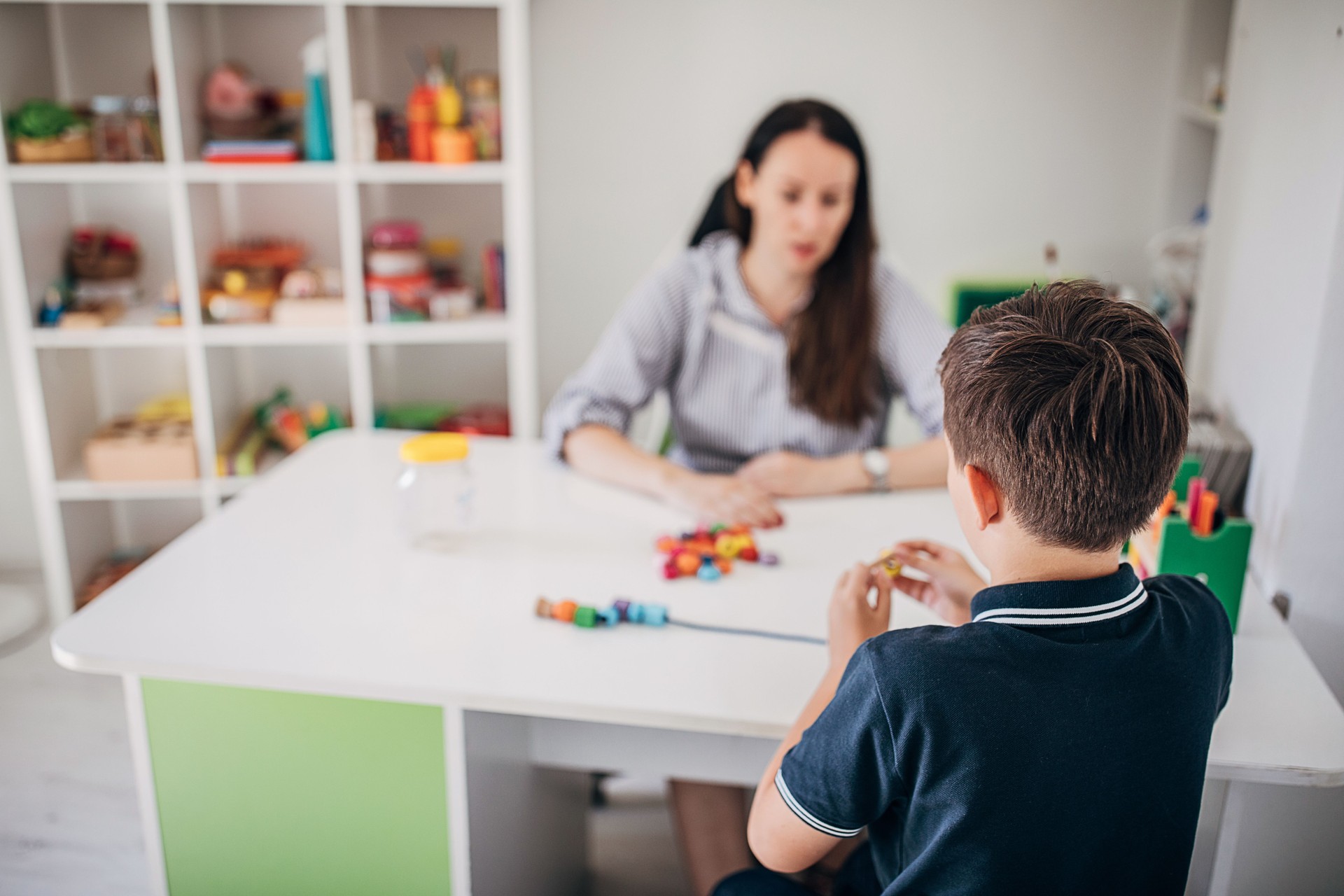 Schoolboy making necklace with his occupational therapist