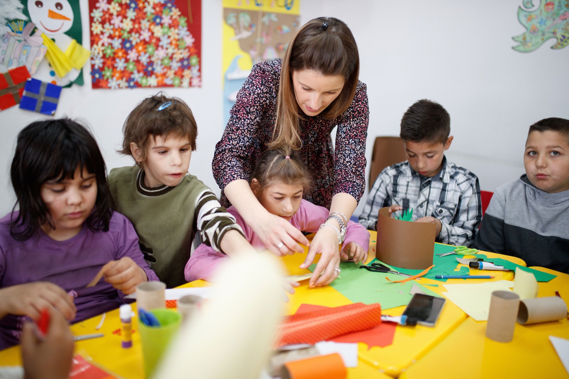 Special education teacher assisting elementary students with paper craft in art class